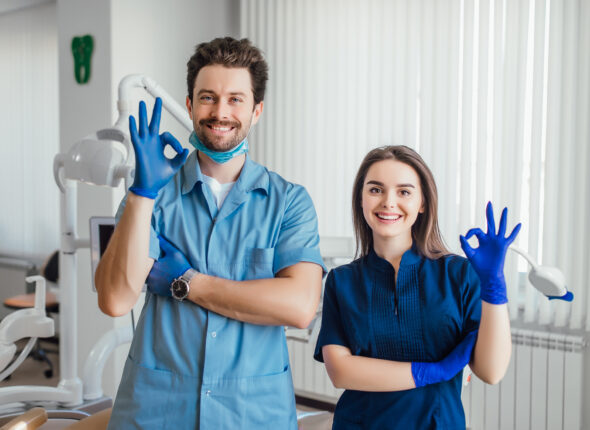 photo-smiling-dentist-standing-with-arms-crossed-with-her-colleague-showing-okay-sign